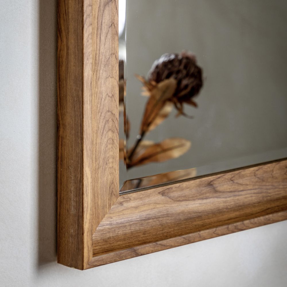 Close-up detail of a walnut wood wall mirror frame featuring clean mitred corners and natural grain texture.
