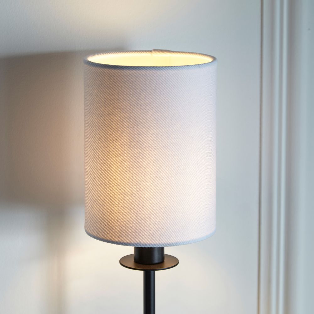 Close-up of a white fabric lampshade on a matte black wall light with warm illuminated glow and contemporary styling.