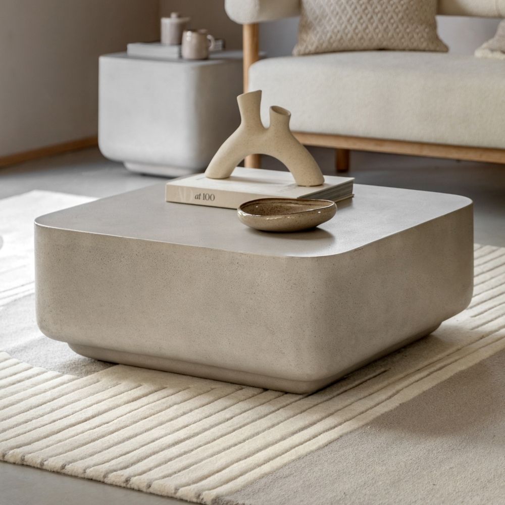 Contemporary concrete effect round coffee table styled in a neutral living room with decorative sculpture, books and soft furnishings.