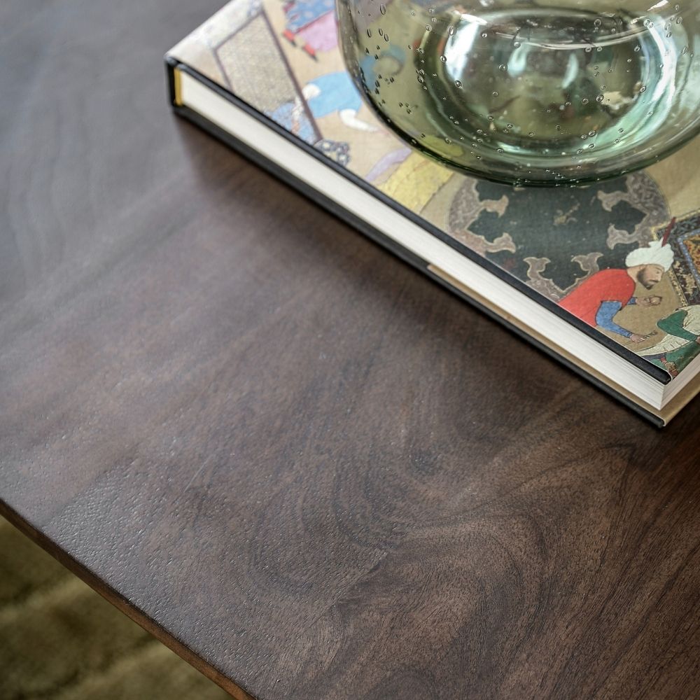 Detailed view of dark mango wood tabletop with natural grain pattern alongside decorative book and glass vase.