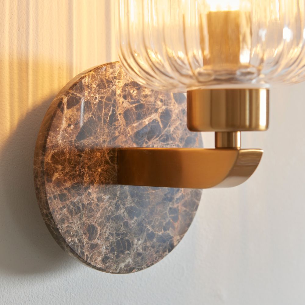Detailed close-up of a dark marble-effect backplate paired with a brushed brass arm on a modern decorative wall light.