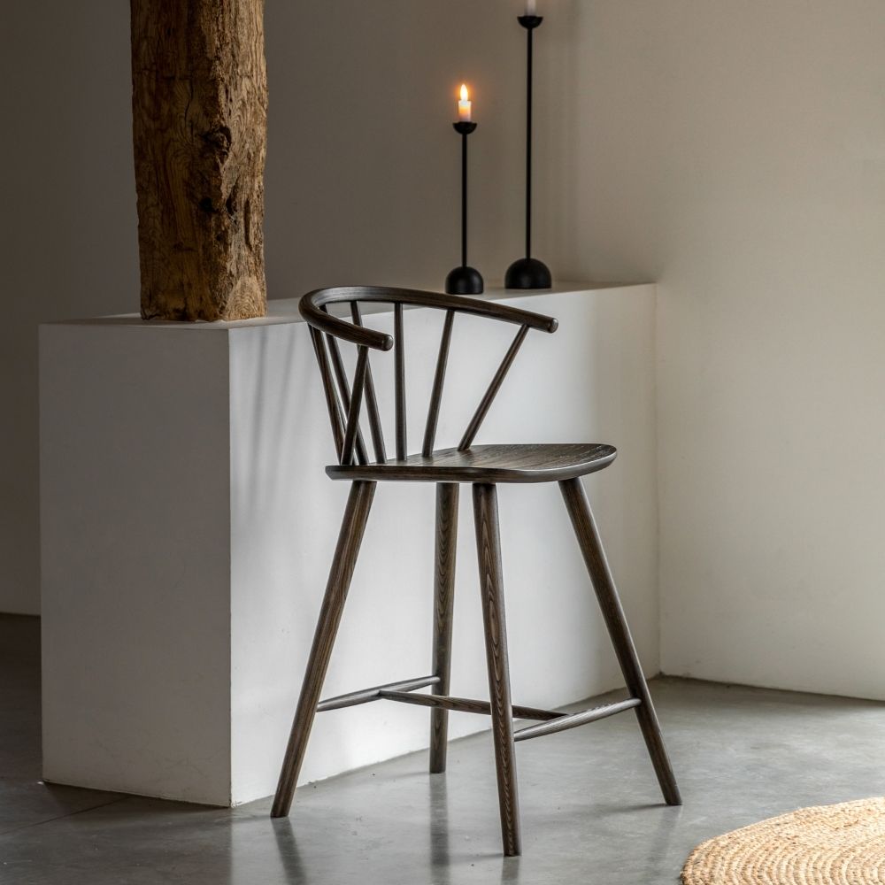 Dark oak spindle back wooden bar stool placed in a minimalist interior with soft lighting, candles and natural textures.