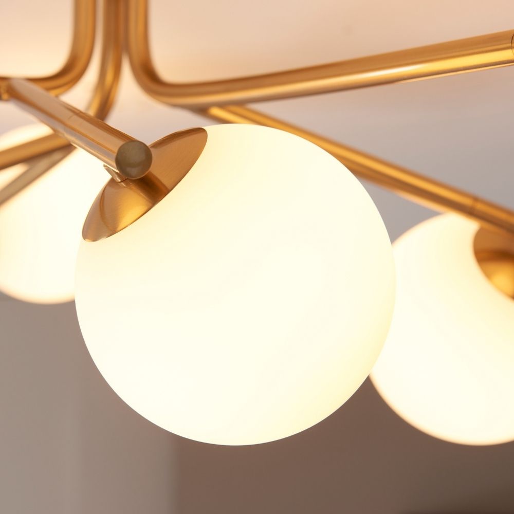 Detailed view of frosted glass globe shade attached to brushed brass arm on a modern ceiling light fitting.