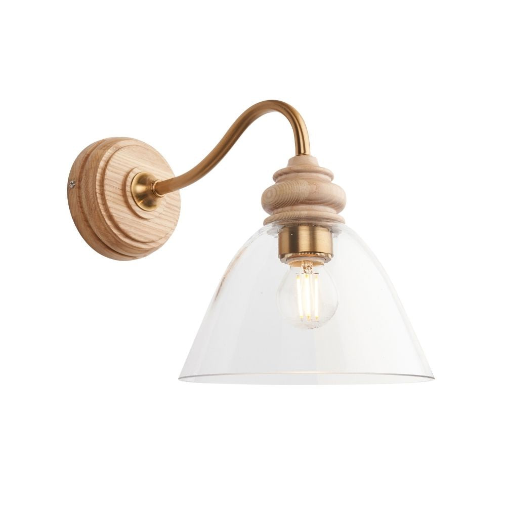 Wall light with clear glass shade, natural ash wood detailing and aged brass arm, showcasing a minimalist contemporary design.