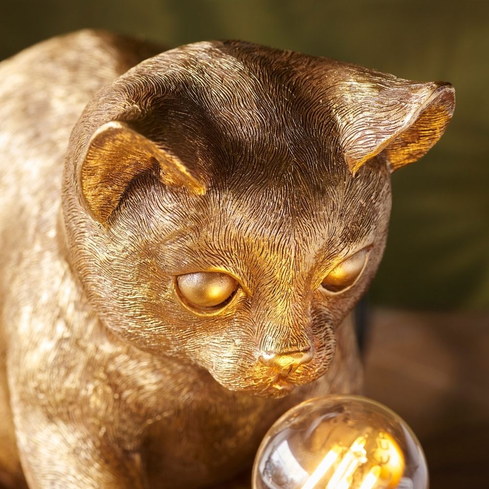 Close-up of gold cat resin lamp showing intricate fur texture and warm glowing filament bulb, highlighting craftsmanship and design detail.