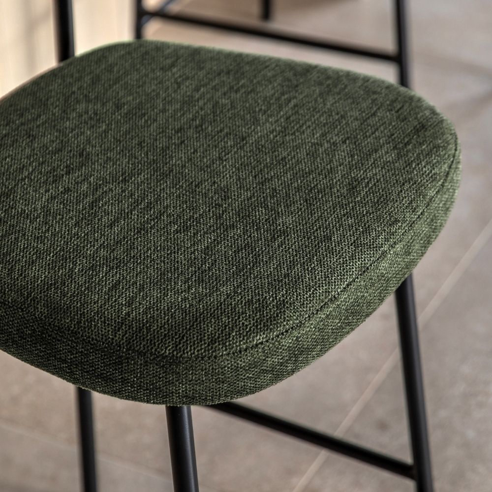Detailed close-up of a green fabric bar stool seat highlighting the soft upholstery texture and black metal frame.