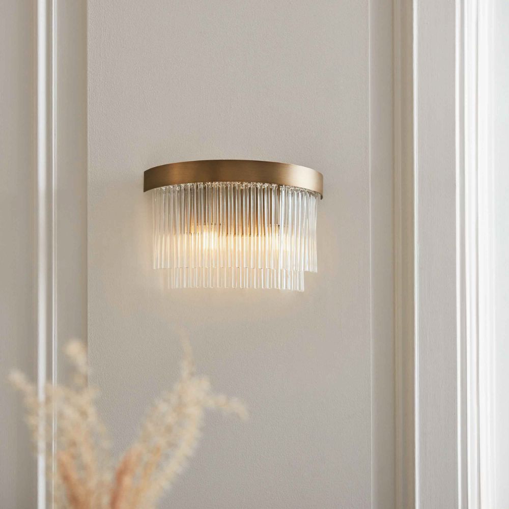 Close-up of a brushed brass wall light with layered clear glass rod detailing.