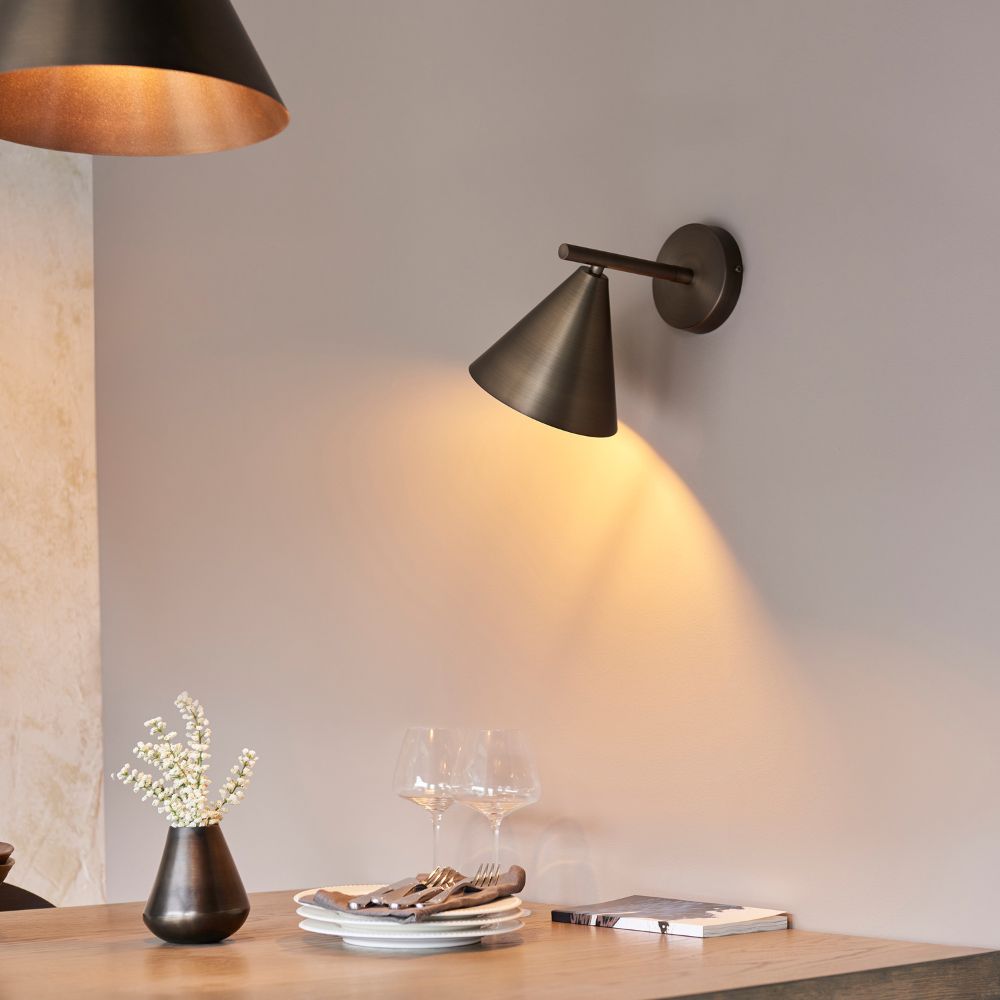 Illuminated bronze cone wall light mounted on a modern interior wall with warm ambient lighting.