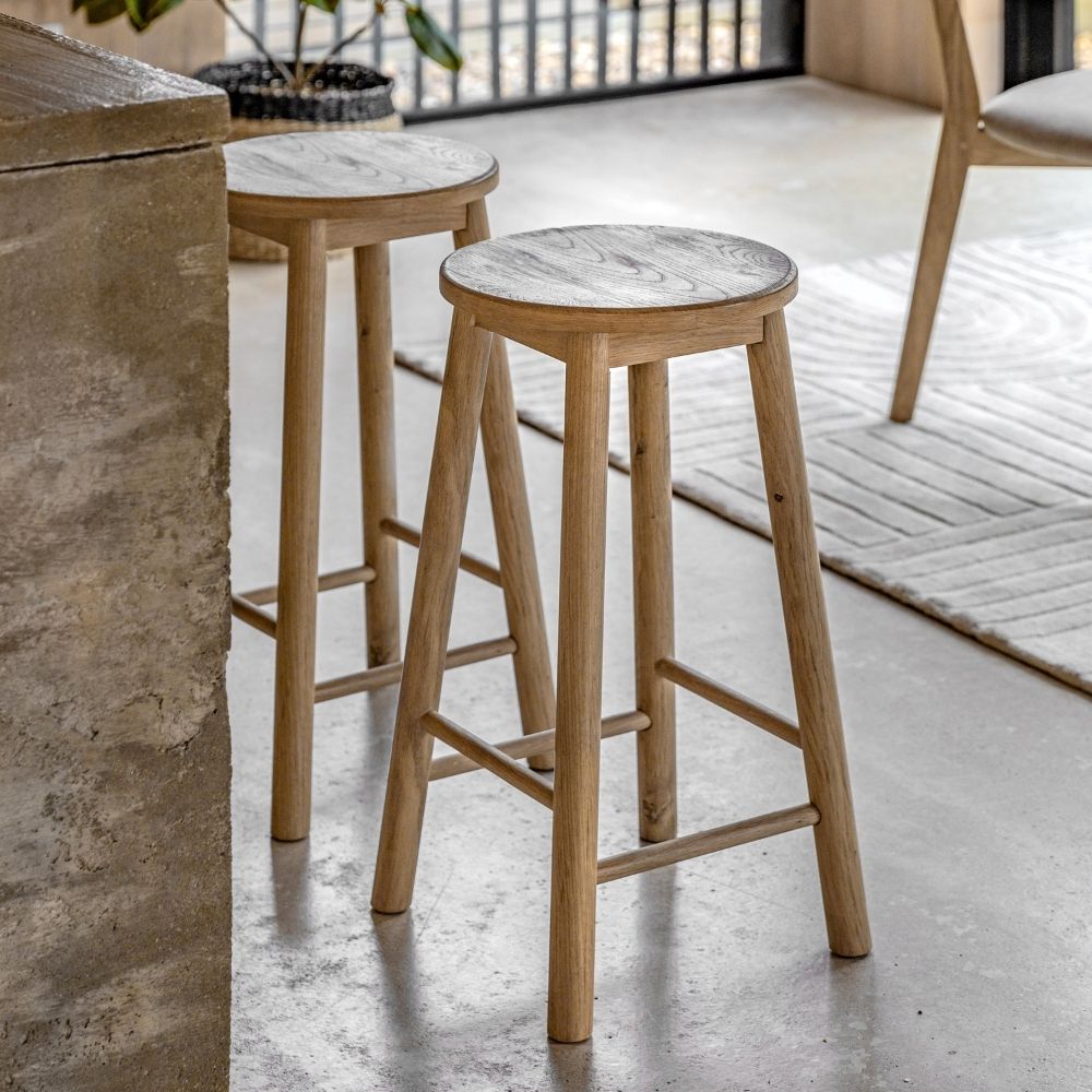Two light oak wooden bar stools placed beside a kitchen island in a modern interior with natural textures and neutral tones.
