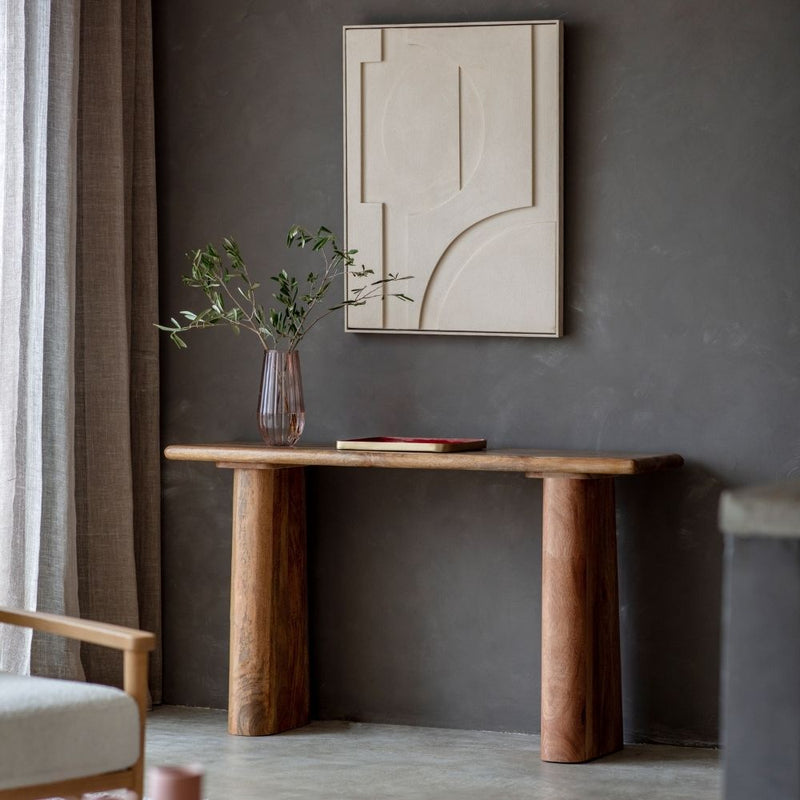 Mango wood curved console table with chunky cylindrical legs styled in a modern interior with wall art, vase and soft neutral tones.