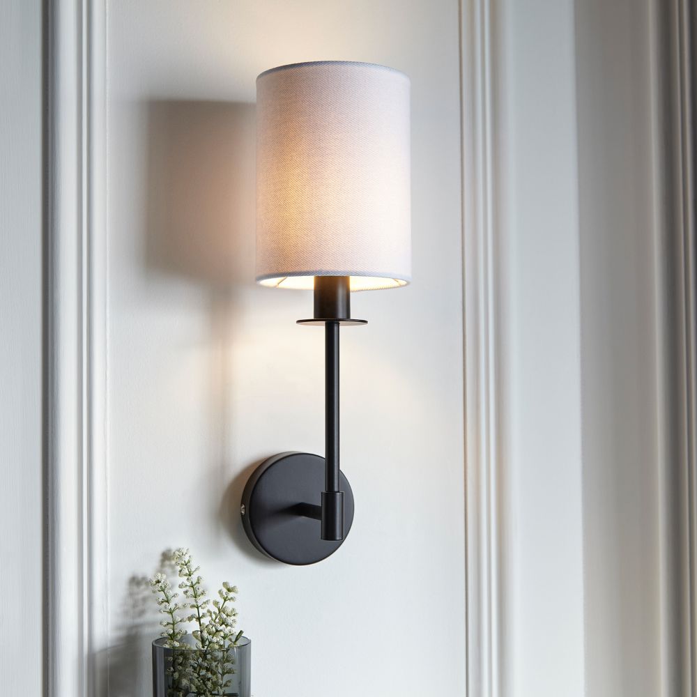 Modern black wall light with a cylindrical white fabric shade, creating soft ambient lighting in a contemporary interior.
