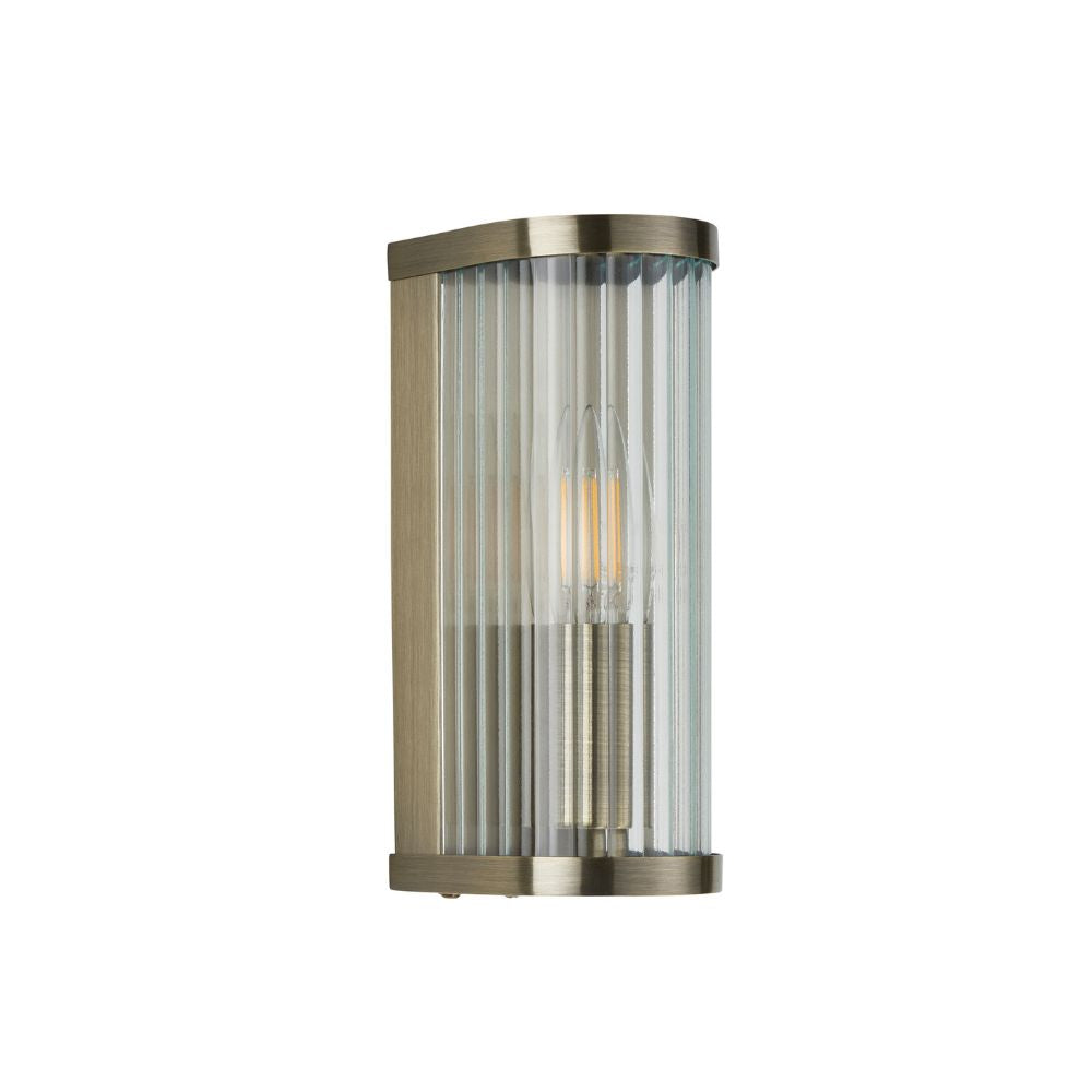 Modern brass wall sconce featuring a fluted glass shade, slim vertical design, and warm decorative illumination.