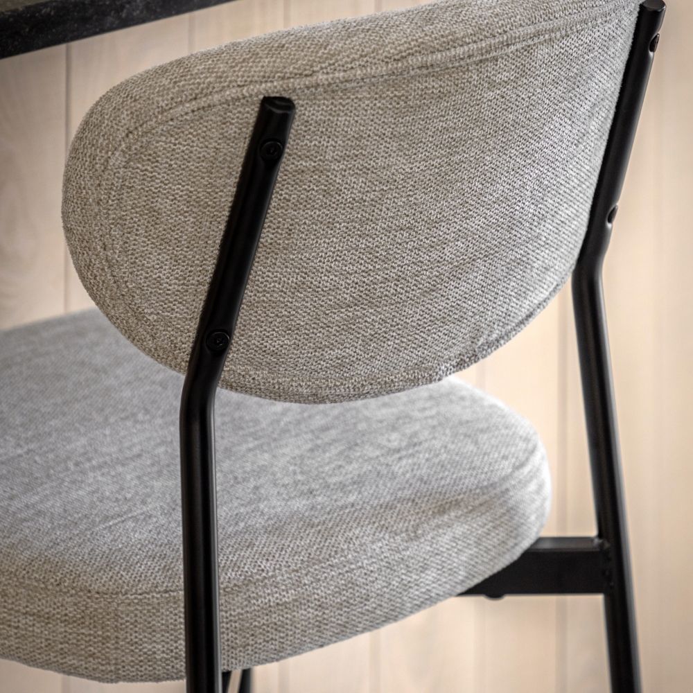 Rear close-up of a natural fabric upholstered bar stool showing the curved backrest, stitching detail and black metal frame.