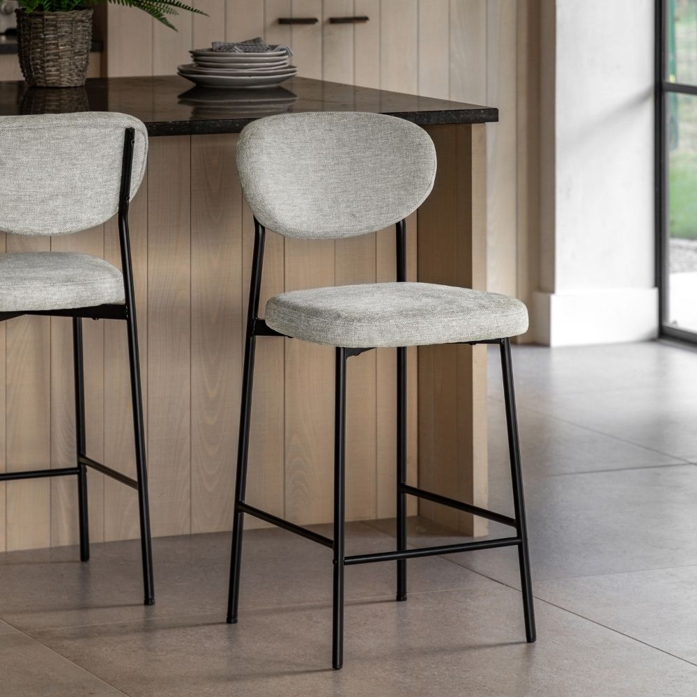 Two natural fabric upholstered bar stools with black metal legs positioned at a kitchen island in a modern interior.