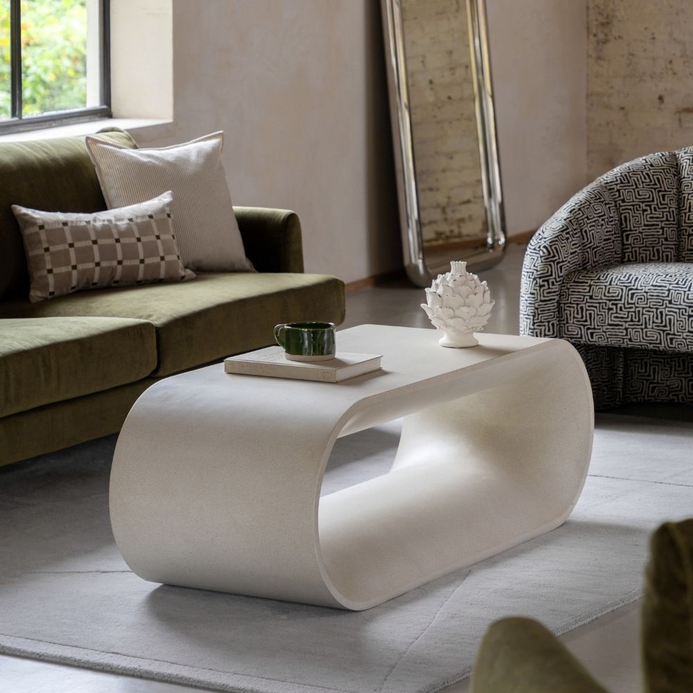 Neutral glass fibre reinforced concrete sculptural coffee table styled in a contemporary living room with sofa, armchair and decorative accessories.