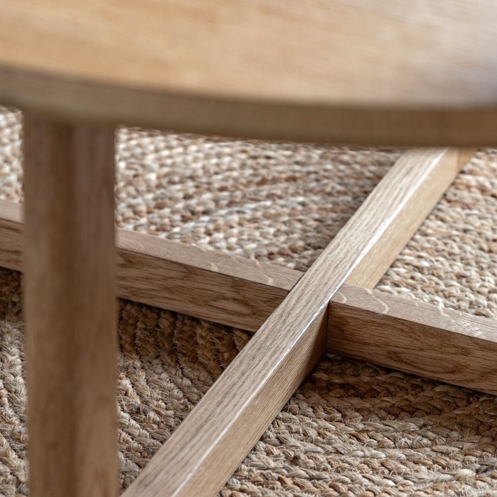 Detailed view of oak coffee table base featuring intersecting supports and curved frame on a textured rug.