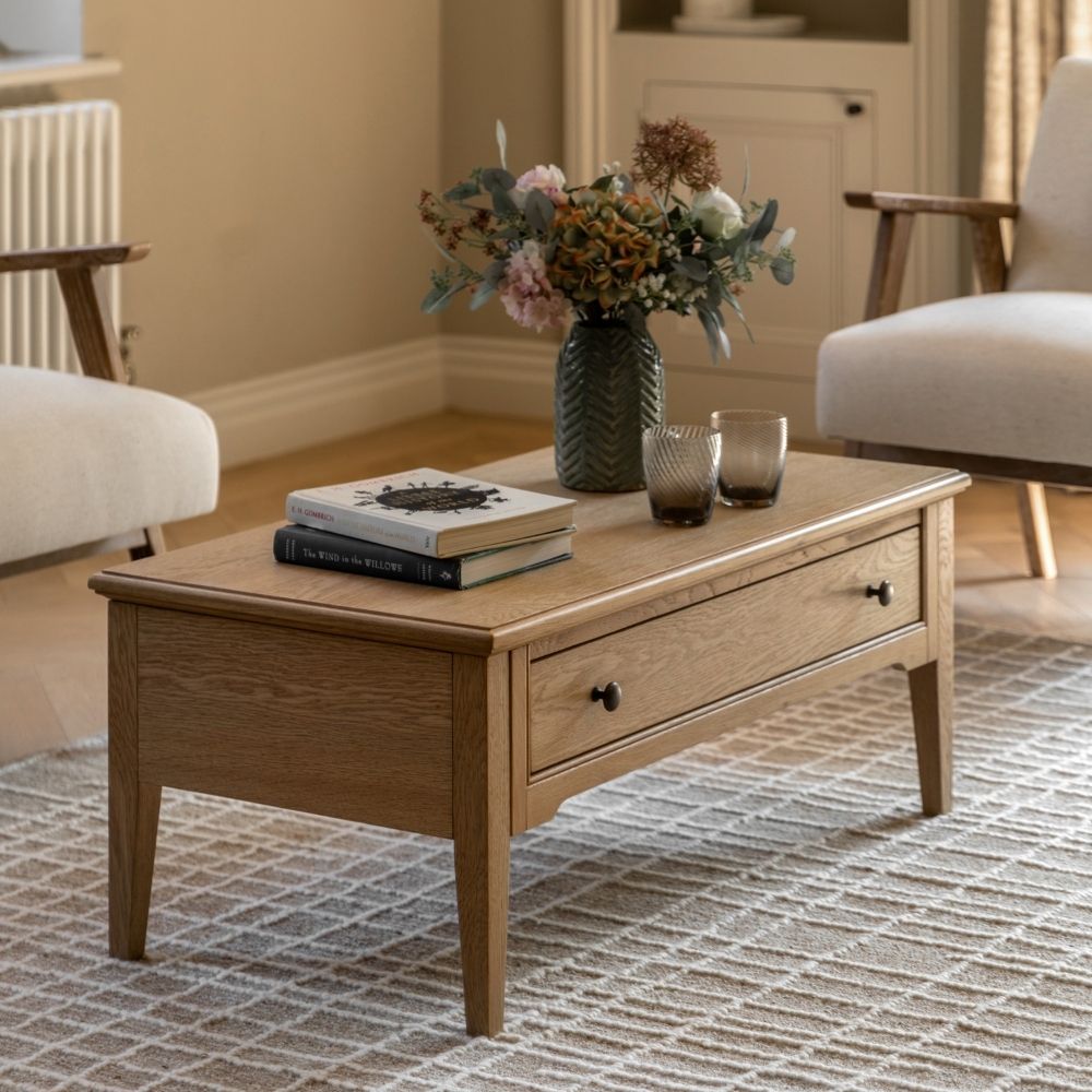 Oak coffee table with built in drawer storage styled in a classic living room with armchairs, rug, books and decorative vase.