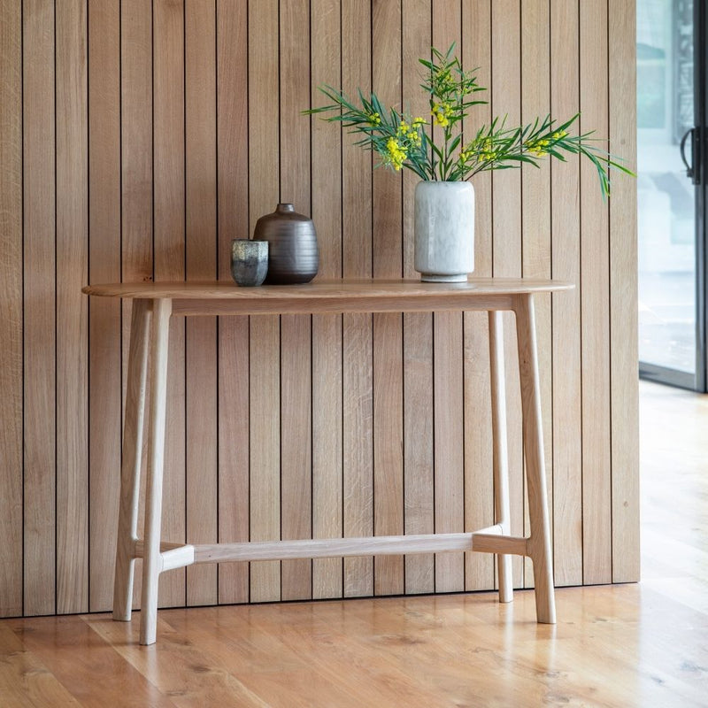 Mid century oak console table with a boat shaped top styled against a wooden panel wall with decorative vases.