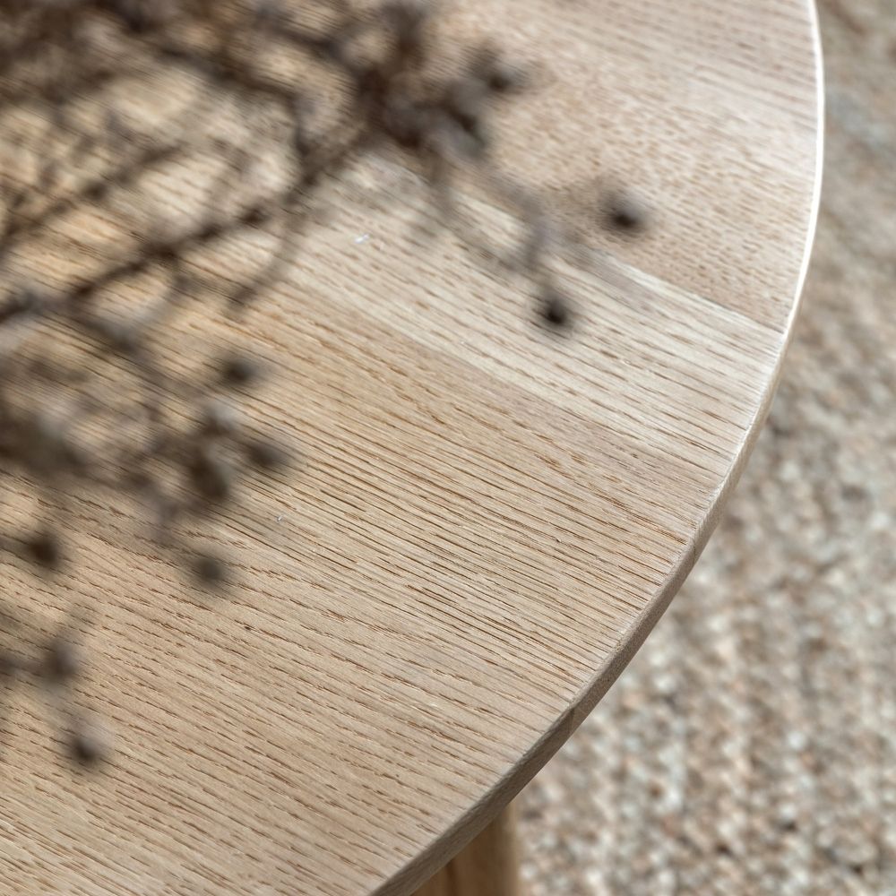 Close up of natural oak tabletop showing fine wood grain and smooth rounded edge in soft lighting.