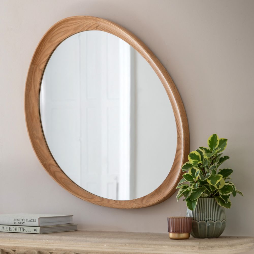 Organic shaped wall mirror with a natural oak wooden frame styled on a neutral console table beside a green houseplant and decorative accessories.