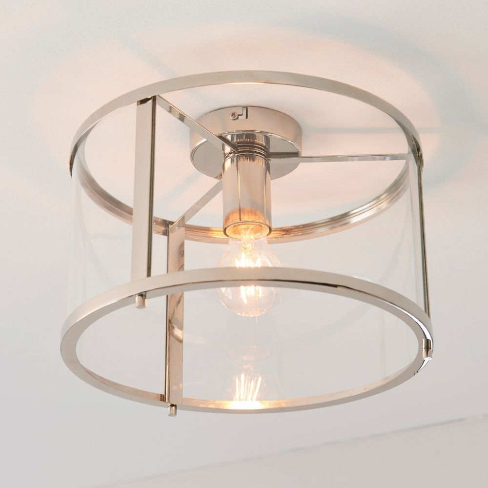 Polished nickel flush ceiling light with clear glass cylindrical shade and exposed filament bulb in a modern interior.