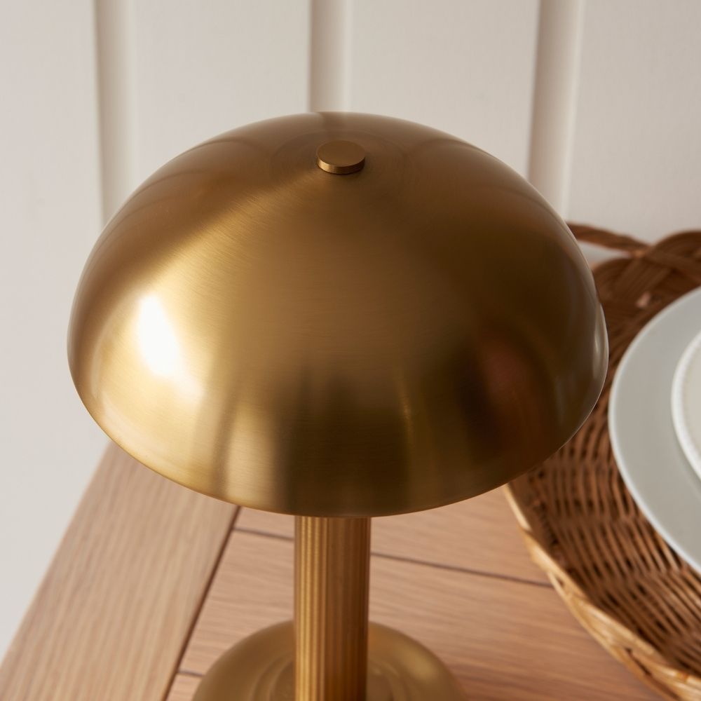 Close-up of rechargeable brass table lamp dome shade with brushed finish, highlighting smooth curves and warm metallic texture on a dining table setting.