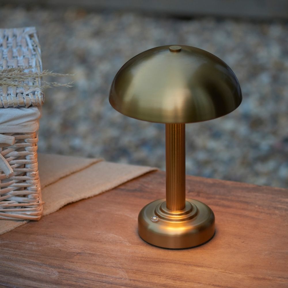 Rechargeable brass touch dimmer table lamp placed outdoors on wooden surface, providing warm ambient lighting with portable wireless design ideal for evening settings.
