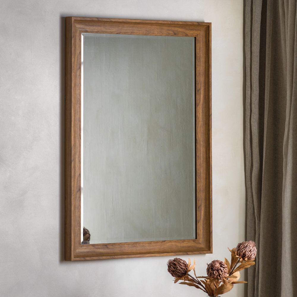 Rectangular wall mirror with a warm walnut wooden frame displayed in a modern neutral interior beside soft curtains and dried floral décor.