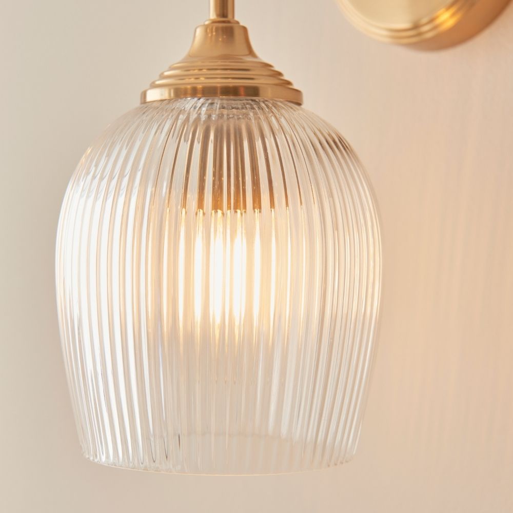 Close-up of ribbed glass shade on a brass wall light, highlighting warm illumination and textured glass design.
