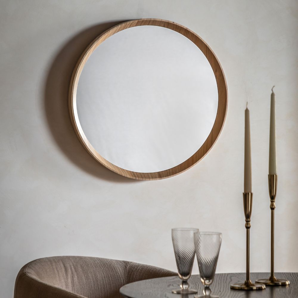 Small round wall mirror with a natural oak frame displayed in a contemporary dining room with neutral décor and brass candlesticks.