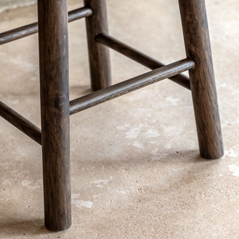 Close-up of smoked oak wooden bar stool legs and footrest showing natural wood grain and sturdy construction on a stone floor.