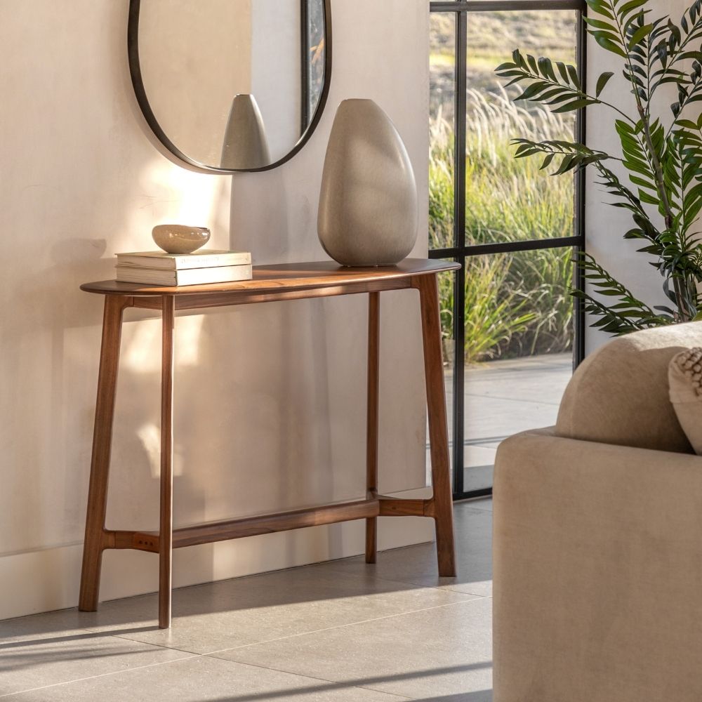 Solid walnut mid century console table with a boat shaped top styled in a modern living space with mirror and decorative accessories.