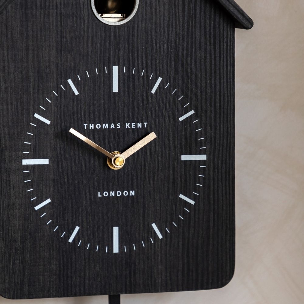Close-up of the Thomas Kent charcoal cuckoo wall clock showing its minimalist white dial markers and gold hands
