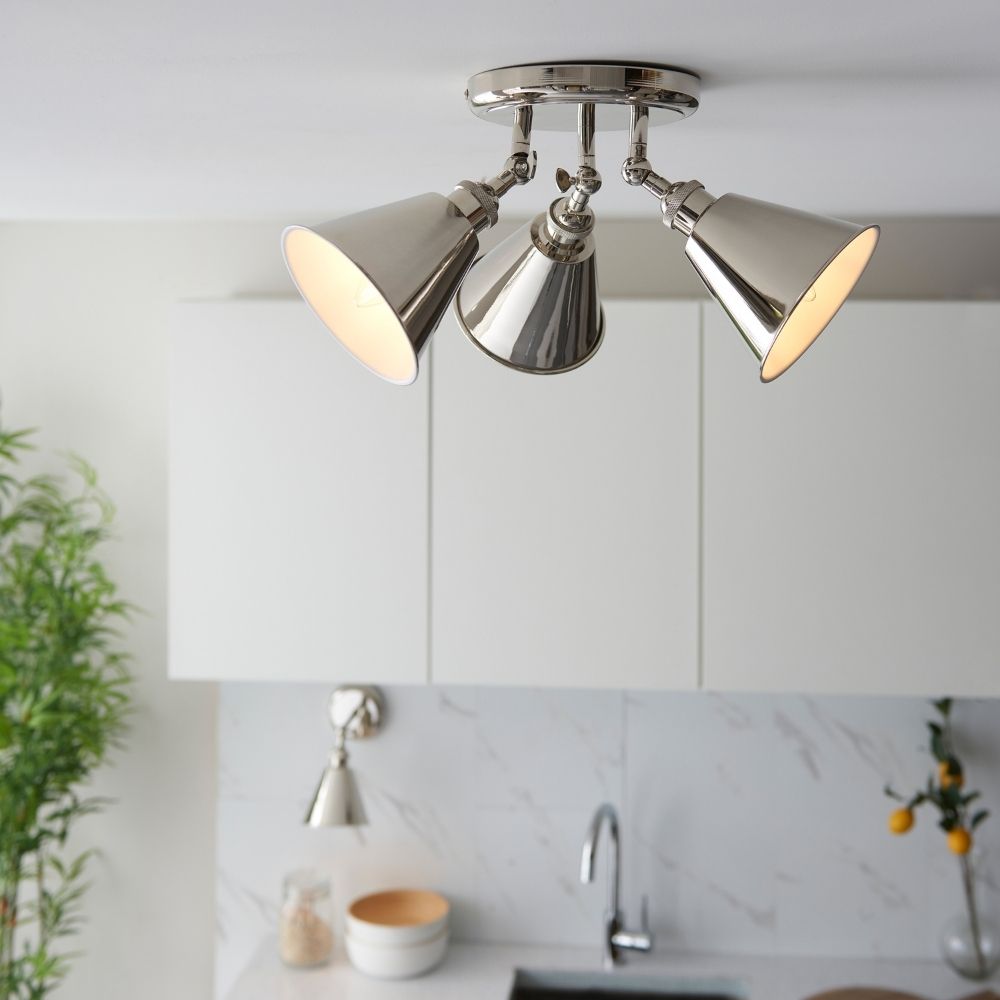 Polished nickel three light spotlight ceiling fixture installed in a modern kitchen with white cabinets and marble backsplash.