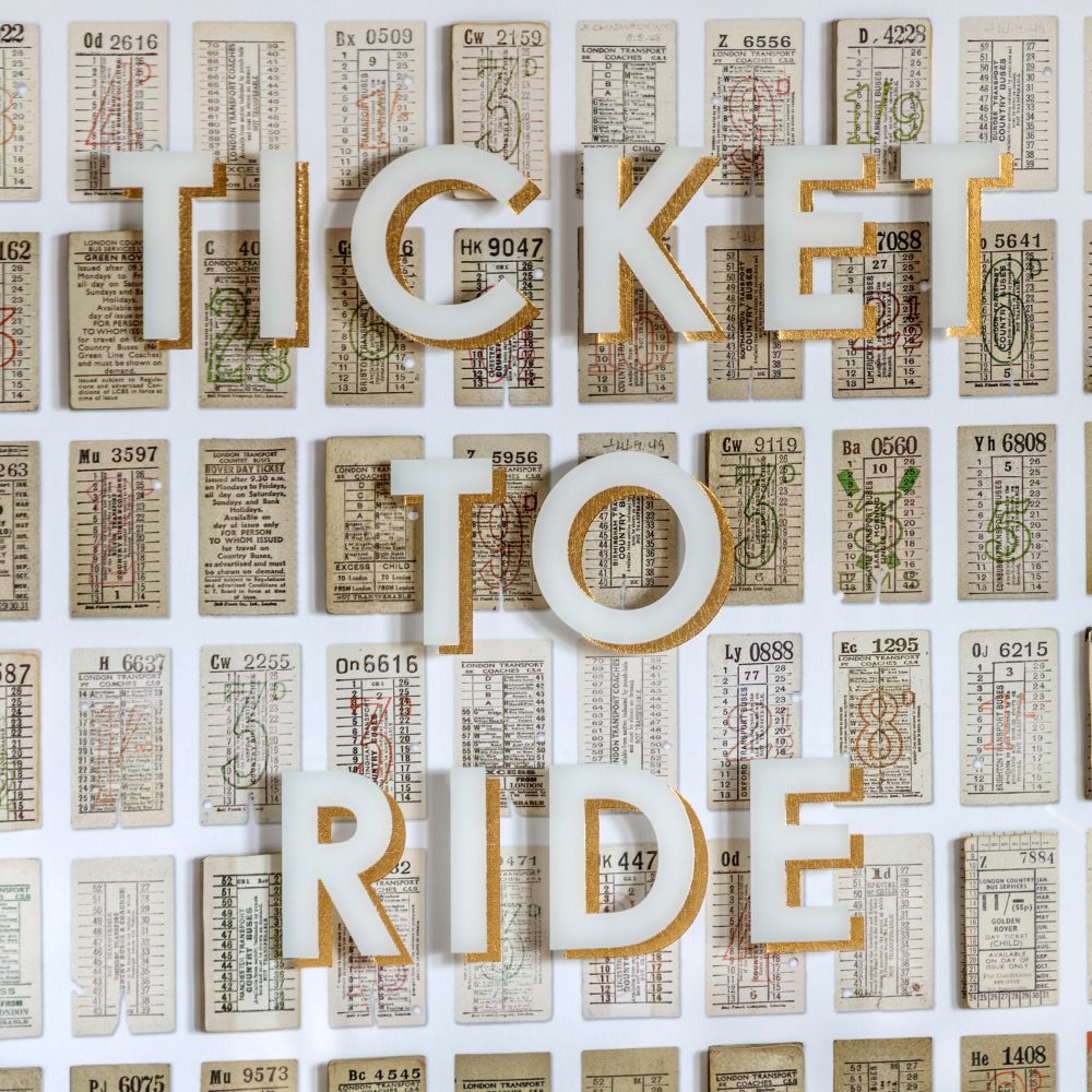Detailed view of Ticket To Ride typographic print featuring gold-edged lettering layered over vintage transport tickets.