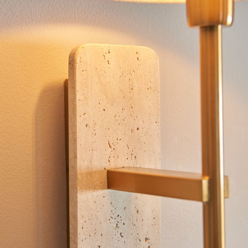 Detailed view of travertine stone backplate with natural porous texture and attached brushed brass arm on wall light.