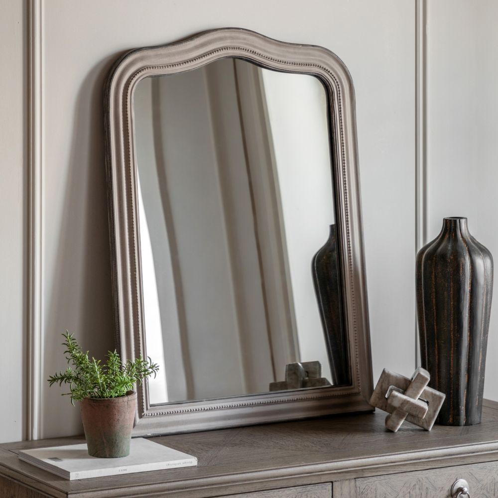 Vintage style arched wall mirror with a distressed grey frame displayed on a wooden console table beside decorative vases and a small plant.