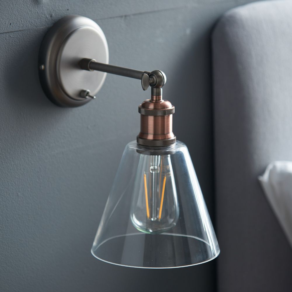 Vintage-style wall light with an exposed LED filament bulb and clear glass shade in a bedroom setting.