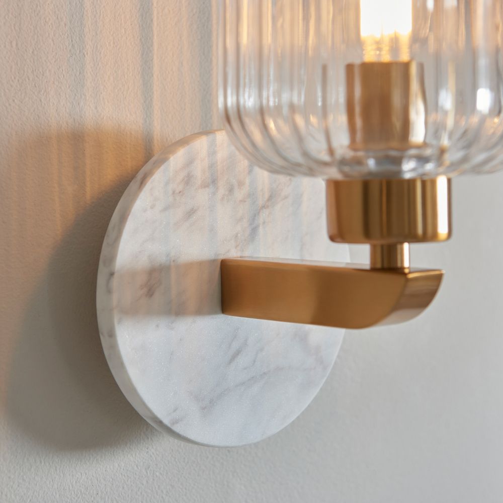 Detailed close-up of a white marble-effect backplate paired with a brushed brass arm on a contemporary decorative wall light.